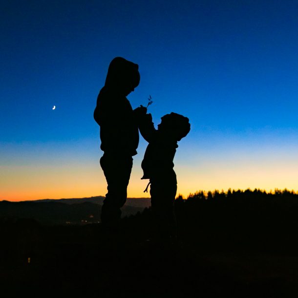 Kind fotografieren lernen - Zwei Kinder halten beim Sonnenuntergang etwas in der Hand - Silhuette